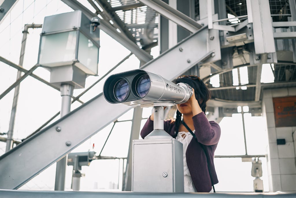 Home 2 A woman uses coin-operated binoculars on a modern outdoor platform.